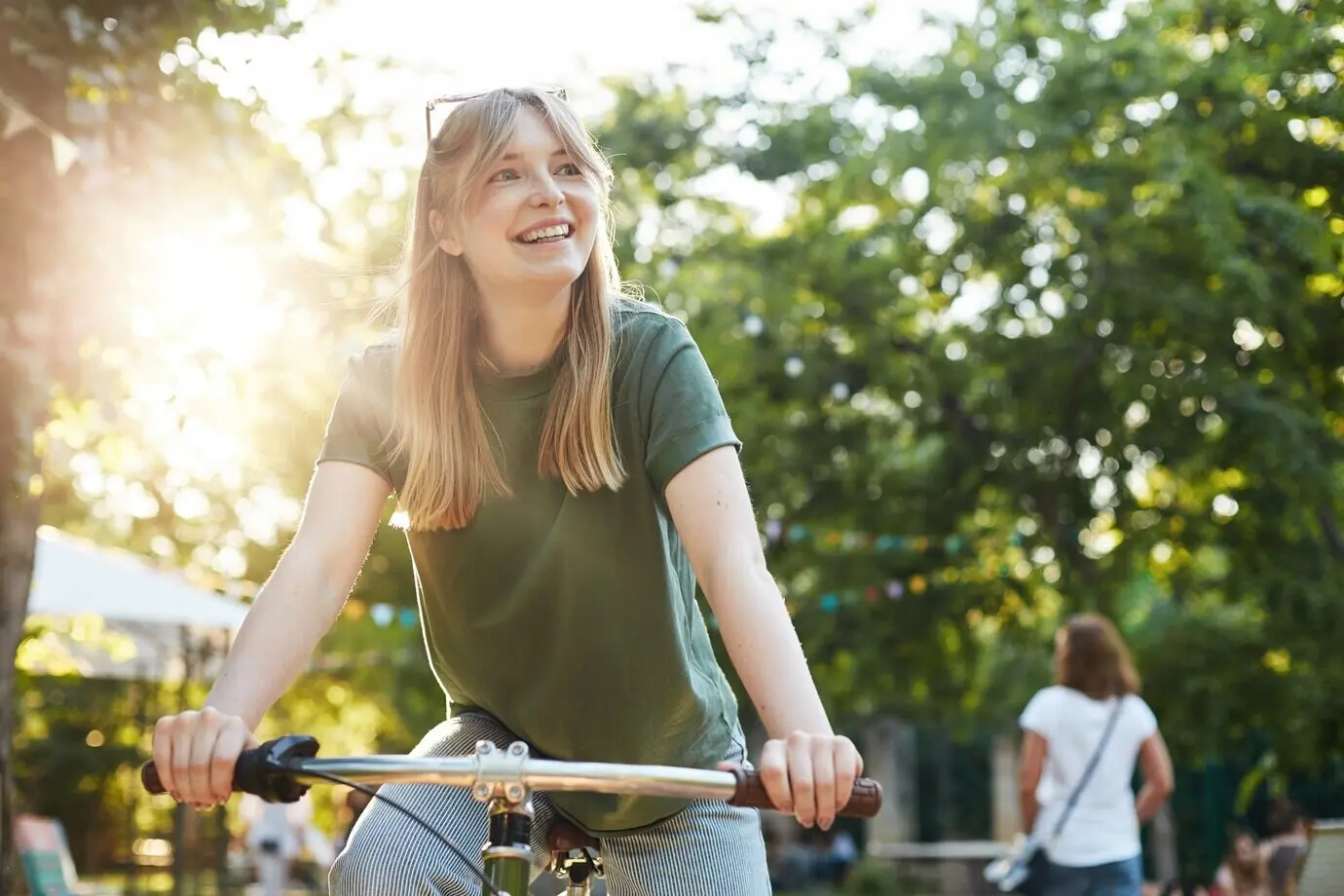 Portrait of a young, beautiful blonde woman happily pretending to ride a bicycle in the park during a food festival.